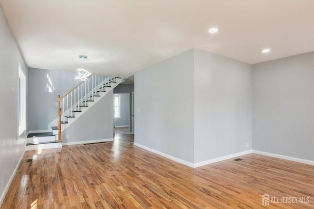 spare room featuring baseboards, a notable chandelier, stairway, and wood finished floors