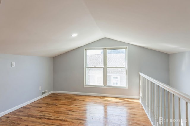 additional living space featuring baseboards, wood finished floors, visible vents, and vaulted ceiling