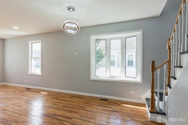 empty room featuring baseboards, wood finished floors, stairway, and a chandelier