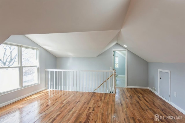 additional living space featuring baseboards, wood finished floors, visible vents, and vaulted ceiling