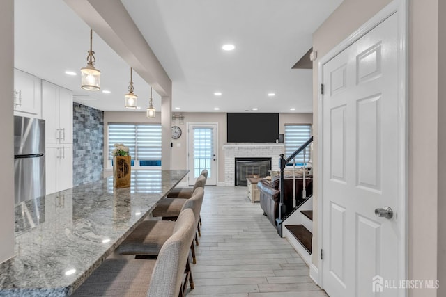 103 Rumford Way, Manalapan, NJ 07726 - kitchen with freestanding refrigerator, white cabinets, light stone counters, light wood finished floors, and a glass covered fireplace