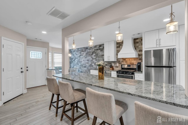 103 Rumford Way, Manalapan, NJ 07726 - kitchen featuring appliances with stainless steel finishes, premium range hood, backsplash, white cabinetry, and a breakfast bar area