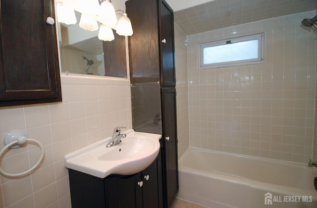 bathroom featuring tasteful backsplash, vanity, tiled shower / bath combo, and tile walls