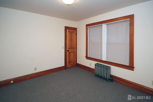 empty room featuring radiator and dark carpet