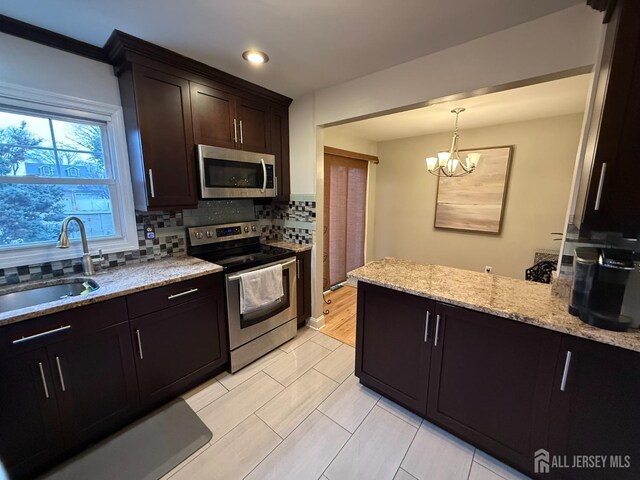 kitchen featuring decorative backsplash, dark brown cabinetry, stainless steel appliances, sink, and an inviting chandelier