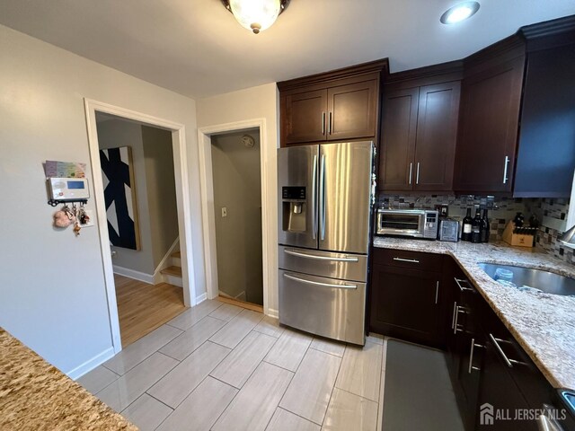 kitchen with sink, light wood-type flooring, tasteful backsplash, light stone counters, and stainless steel fridge with ice dispenser