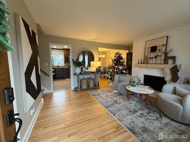 living room featuring light wood-type flooring, a brick fireplace, brick wall, sink, and a notable chandelier