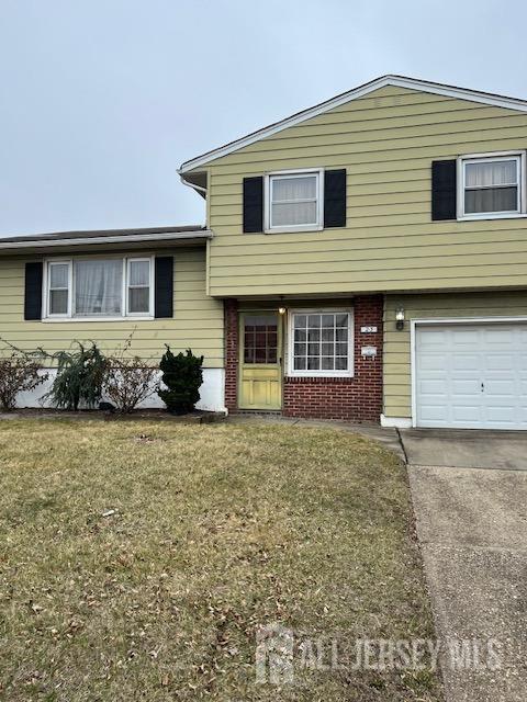 split level home featuring concrete driveway, brick siding, a front yard, and a garage