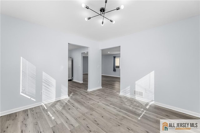 unfurnished room with baseboards, visible vents, a chandelier, and wood finished floors