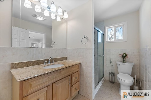 bathroom with tile patterned flooring, toilet, tile walls, and a shower stall