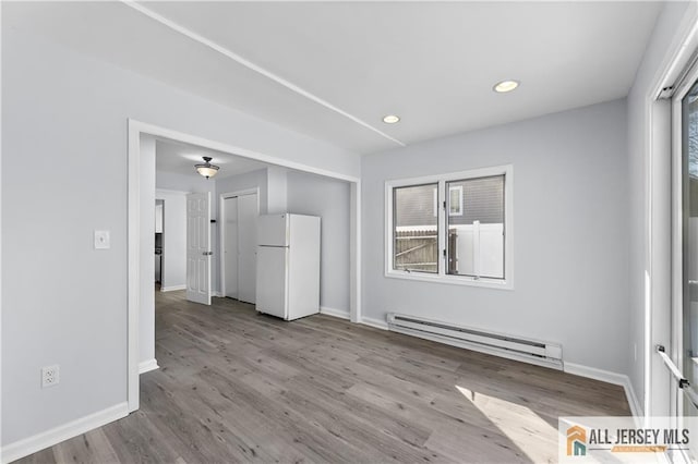 empty room featuring a baseboard heating unit, recessed lighting, baseboards, and wood finished floors