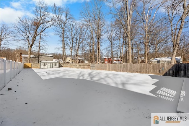 yard layered in snow with a storage shed, a fenced backyard, and an outbuilding