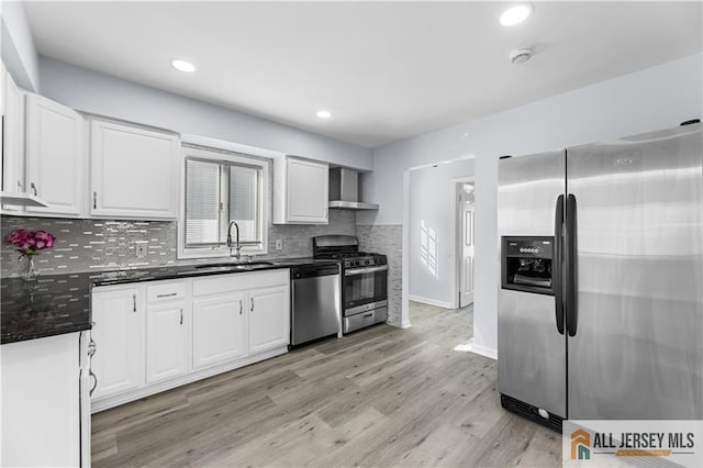 kitchen featuring a sink, white cabinetry, appliances with stainless steel finishes, wall chimney exhaust hood, and dark countertops