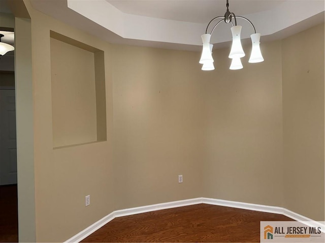 empty room featuring a notable chandelier, dark wood finished floors, and baseboards