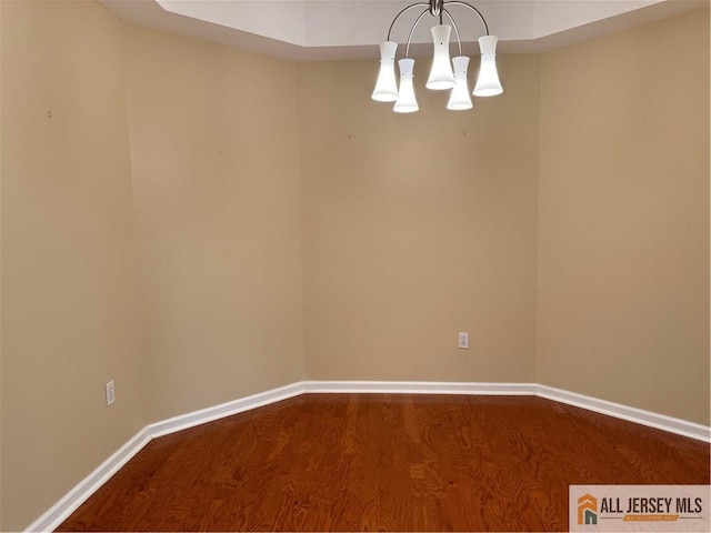 unfurnished room with dark wood-type flooring, baseboards, and an inviting chandelier