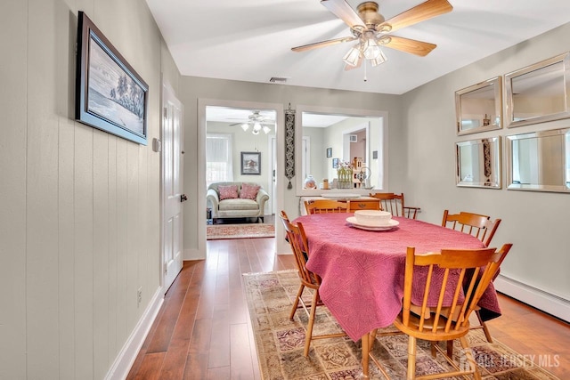 dining room featuring a baseboard radiator, ceiling fan, visible vents, hardwood / wood-style floors, and baseboards