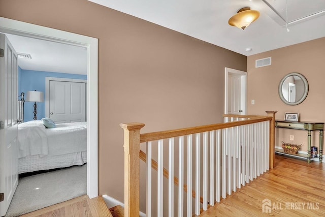 hall with attic access, an upstairs landing, visible vents, and wood finished floors