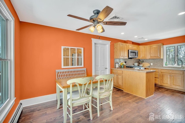kitchen with stainless steel microwave, a sink, a baseboard radiator, visible vents, and light brown cabinetry