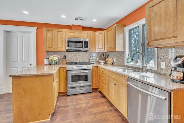 kitchen featuring light brown cabinetry, appliances with stainless steel finishes, a sink, visible vents, and a peninsula