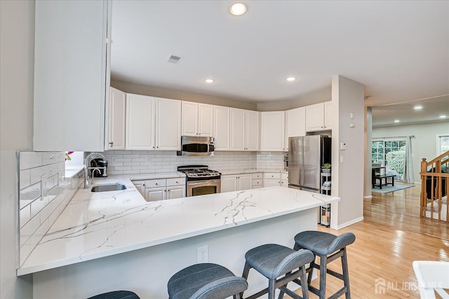 kitchen featuring a kitchen bar, sink, white cabinetry, appliances with stainless steel finishes, and kitchen peninsula