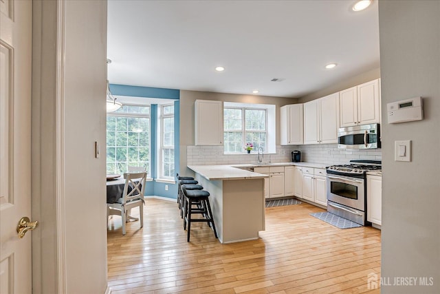 kitchen featuring appliances with stainless steel finishes, white cabinetry, a breakfast bar area, backsplash, and kitchen peninsula