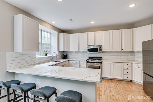 kitchen featuring light stone counters, stainless steel appliances, kitchen peninsula, and white cabinets