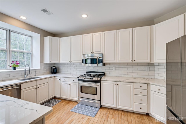 kitchen with tasteful backsplash, white cabinetry, sink, stainless steel appliances, and light stone countertops