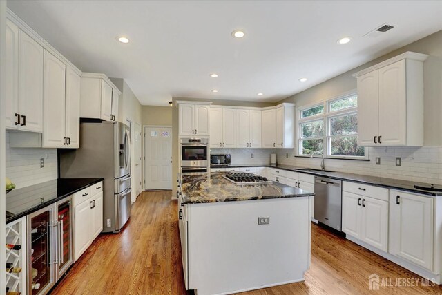 kitchen featuring sink, light hardwood / wood-style flooring, dark stone countertops, white cabinets, and appliances with stainless steel finishes