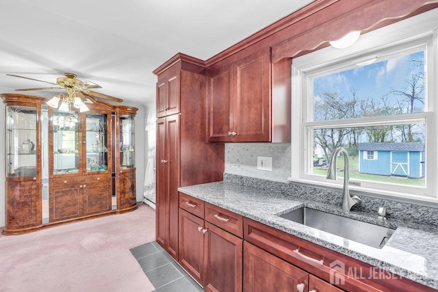 kitchen with a sink, light stone counters, a ceiling fan, and backsplash