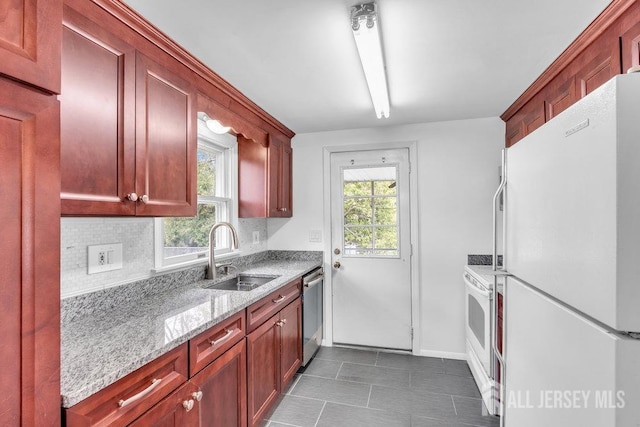 kitchen featuring freestanding refrigerator, a sink, stainless steel dishwasher, light stone countertops, and dark tile patterned flooring