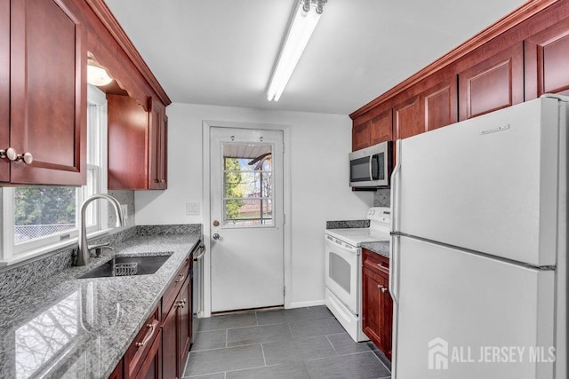 kitchen with stainless steel appliances, a sink, dark brown cabinets, light stone countertops, and dark tile patterned flooring