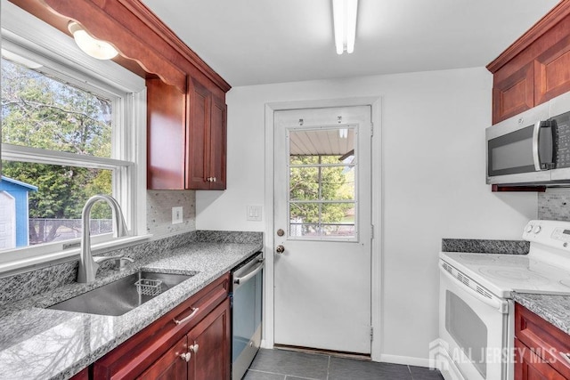 kitchen with appliances with stainless steel finishes, dark brown cabinets, a sink, decorative backsplash, and dark tile patterned flooring