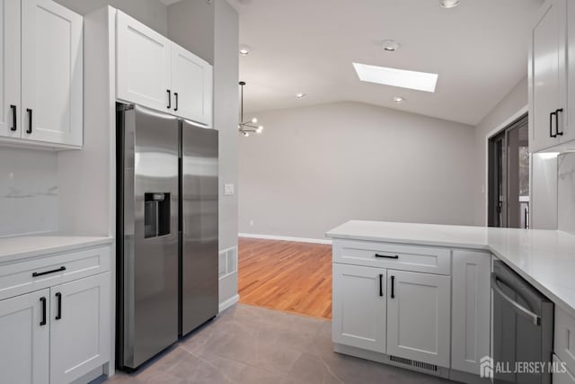 kitchen with lofted ceiling with skylight, light countertops, a peninsula, white cabinets, and stainless steel appliances