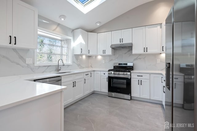 kitchen featuring under cabinet range hood, light countertops, vaulted ceiling with skylight, appliances with stainless steel finishes, and a sink