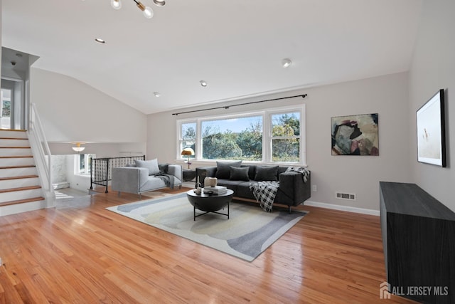 living room with visible vents, stairway, light wood-style floors, baseboards, and vaulted ceiling