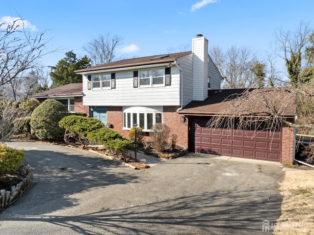 view of front facade featuring brick siding, driveway, a chimney, and a garage