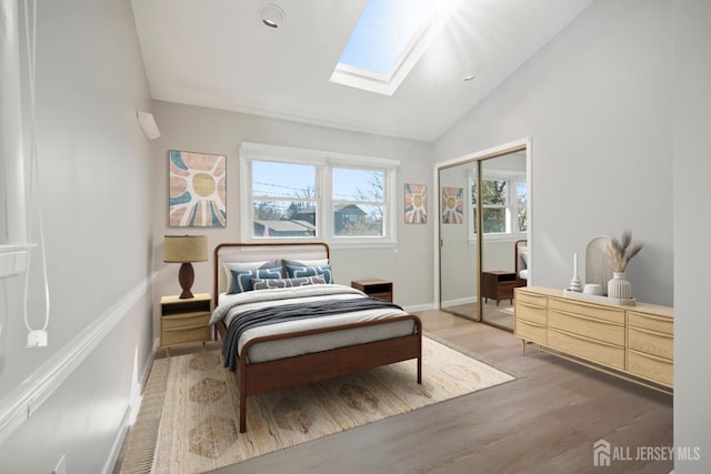 bedroom with vaulted ceiling with skylight, baseboards, light wood-type flooring, and a closet