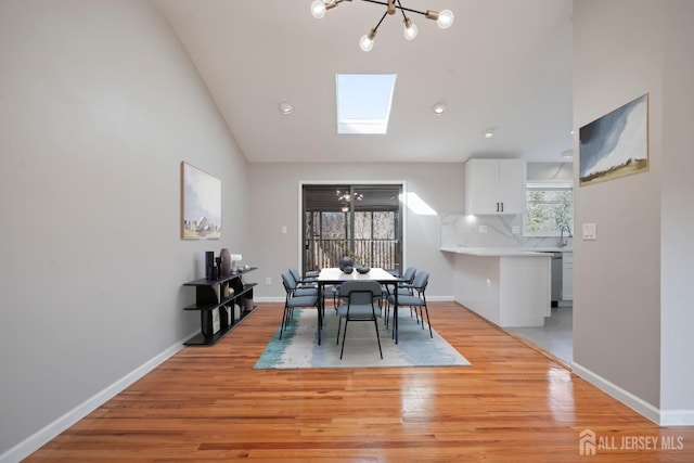 dining room with lofted ceiling with skylight, baseboards, light wood finished floors, and a chandelier