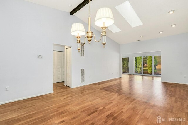 spare room featuring a skylight, beam ceiling, hardwood / wood-style flooring, an inviting chandelier, and high vaulted ceiling