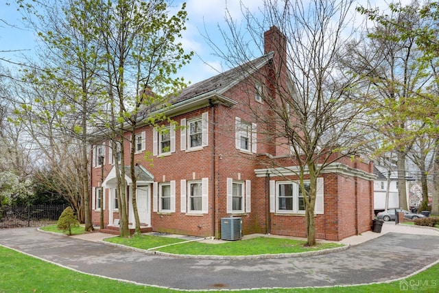 view of property exterior featuring fence, a yard, brick siding, central AC unit, and a chimney