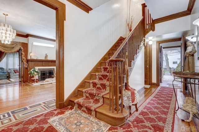 stairs with a glass covered fireplace, a notable chandelier, wood finished floors, and ornamental molding