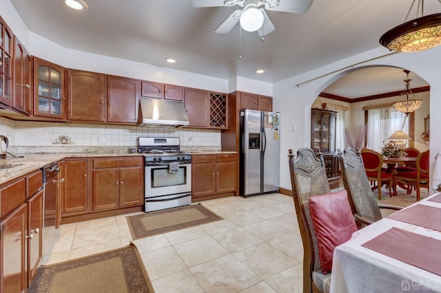 kitchen with under cabinet range hood, tasteful backsplash, stainless steel appliances, arched walkways, and light stone countertops