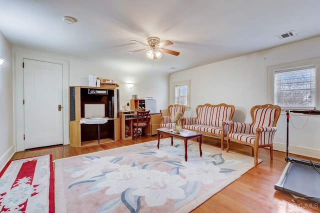 living area featuring baseboards, wood finished floors, visible vents, and ceiling fan