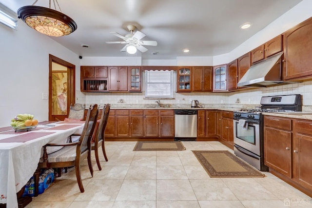 kitchen with under cabinet range hood, decorative backsplash, stainless steel appliances, and glass insert cabinets