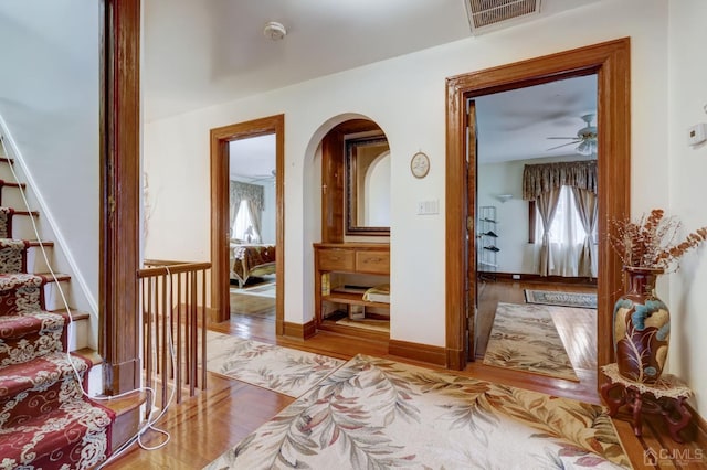 hall featuring visible vents, wood finished floors, stairway, arched walkways, and baseboards