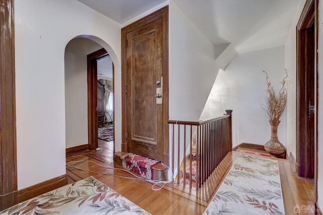 corridor featuring baseboards, arched walkways, and wood finished floors