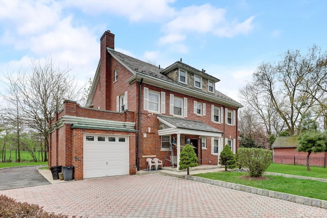 american foursquare style home with decorative driveway, brick siding, a chimney, and fence