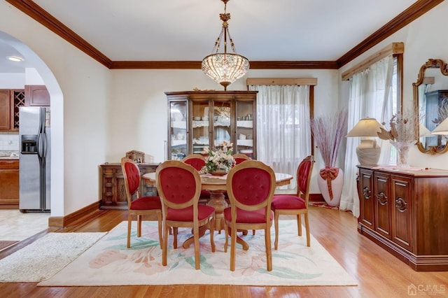 dining space featuring arched walkways, light wood-style flooring, crown molding, and baseboards