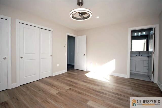 unfurnished bedroom with ensuite bathroom, wood-type flooring, and sink