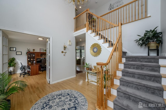 foyer entrance featuring a towering ceiling, an inviting chandelier, wood finished floors, baseboards, and stairs